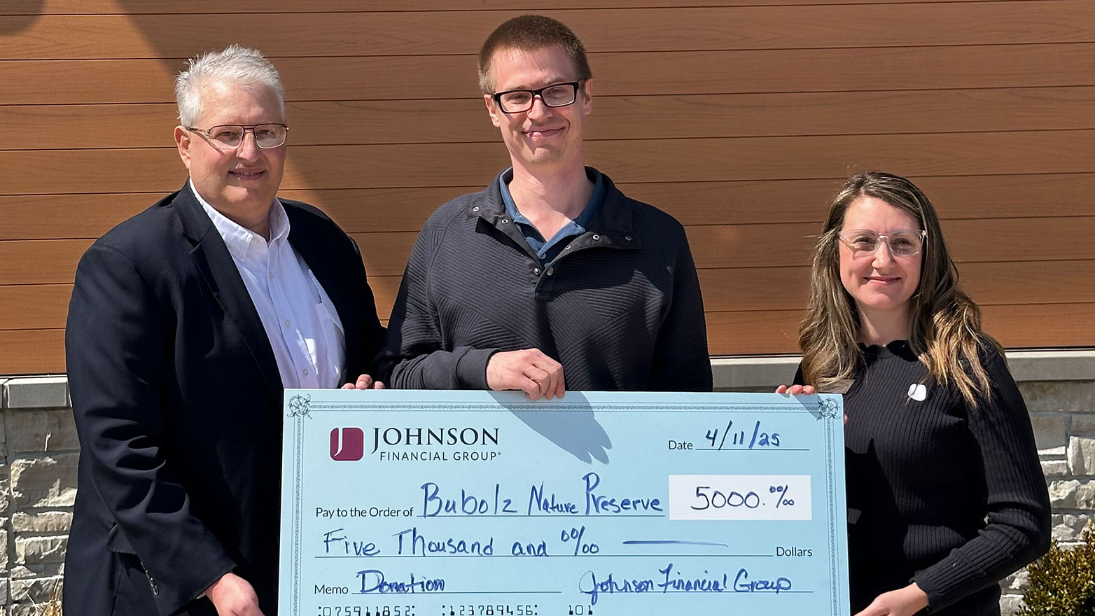 Three individuals from Bubolz Nature Preserve hold a large check for $5,000, a donation from Johnson Financial Group.