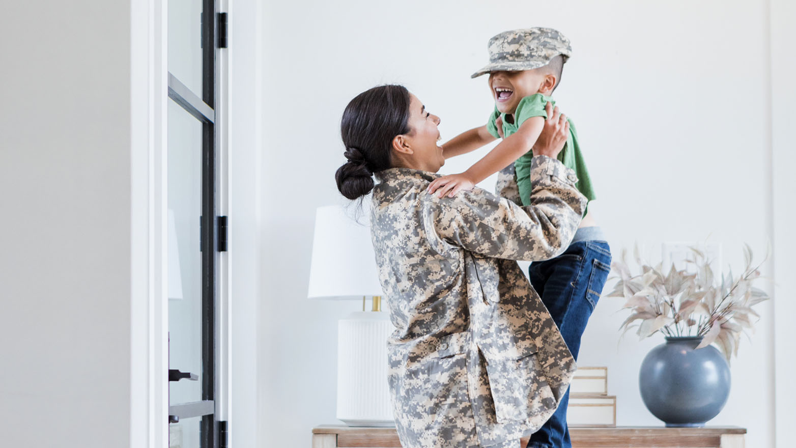 A heartwarming embrace between a mother in uniform and her giggling child, donning a matching cap.